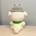 Fluffy plush sculpture of a white dog with black beaded eyes and wire framed glasses. It wears a green scarf and has a camera around its neck and a Totoro hat.