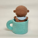 Crocheted otter plush inside a teal mug with a pink heart on a white background