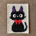 Crocheted black cat with purple ears and a red bow tie on a beige background