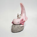 Pink axolotl figurine with a small white creature on a gray stone base against a light gray background. 
