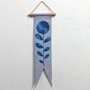 Painting on a long, thin banner of a blue flower with leaves and a long, thin stem. 