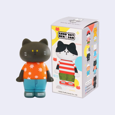 Vinyl figure of a black cat standing and wearing an orange shirt and jeans. It stands next to its product packaging.