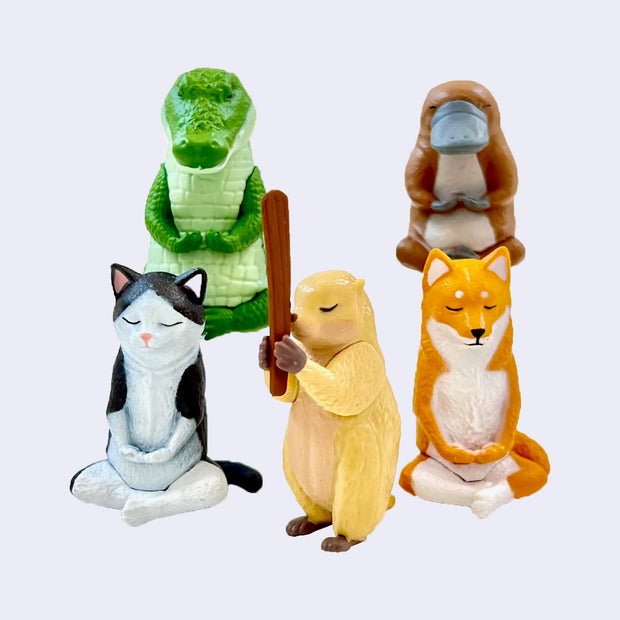 5 different plastic figures of animals sitting cross legged in meditative positions. Options are: crocodile, platypus, cat, fox and a gopher holding a wooden stick.