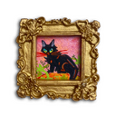 A small framed art print featuring a black cat with green eyes and orange markings on a pink background, set within an ornate gold frame.
