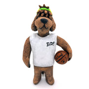 Sculpture of a fluffy tan dog with shaggy hair over its eyes. It stands like a human and wears a white tank top, a green backwards cap and holds a basketball under its arm.