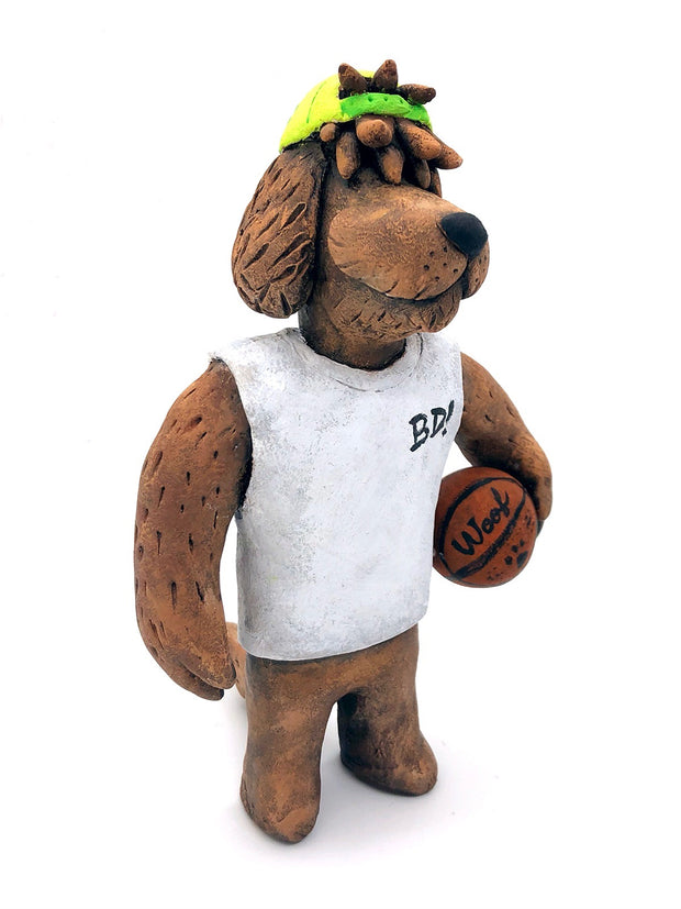 Sculpture of a fluffy tan dog with shaggy hair over its eyes. It stands like a human and wears a white tank top, a green backwards cap and holds a basketball under its arm.