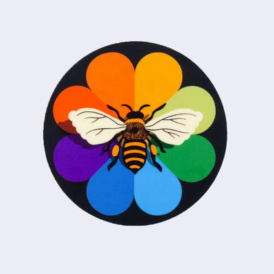 Circular sticker of a bee on a rainbow colored rainbow, with a solid black background.