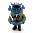 Clay sculpture of a blue robot wearing glasses with a black baseball cap, green army jacket and holding a camera in both hands and a magazine in between its arm.