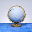 A globe, painting entirely light blue with a closed eye, calm facial expression. Small white wooden flowers are attached at opposite corners of the globe.