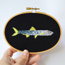 Embroidery of a fish on black fabric held in an embroidery hoop.