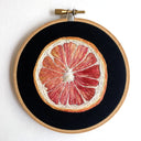 Embroidered grapefruit cross section, on black background in wooden embroidery hoop.