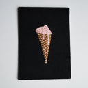 Embroidery of a pink ice cream cone on a black textured surface with a light gray background