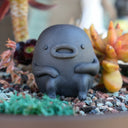 Gray vase with a cute monster face and arms and legs.