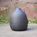 Gray vase with a cute monster face and arms and legs.