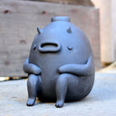 Gray vase with a cute monster face and arms and legs.