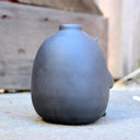 Gray vase with a cute monster face and arms and legs.