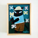 Framed artwork of a black cat with a hat and surprised expression, surrounded by butterflies on a blue background.