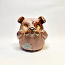 Ceramic sculpture of a cute, brown bulldog with its paws on its cheek and a rounded bottom without legs.