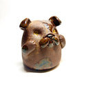 Ceramic sculpture of a cute, brown bulldog with its paws on its cheek and a rounded bottom without legs.