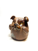 Ceramic sculpture of a cute, brown bulldog with its paws on its cheek and a rounded bottom without legs.