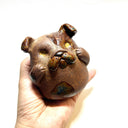 Ceramic sculpture of a cute, brown bulldog with its paws on its cheek and a rounded bottom without legs.