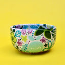 Small ceramic bowl, white with many paintings of floral patterns and fruits in cool tones such as green, blue and purple.