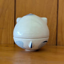 Ceramic sculpture of a blue cat jar, with a shallow bowl for the bottom and a cat head for the lid. The cat has simply drawn patterning, ears and closed eyes with thick eyeliner.