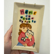 Rectangular ceramic tray with a painting in the inner dish of a girl holding a white cartoon dog. Colorful text overhead reads "Home is where my dog is"
