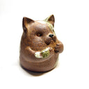 Ceramic sculpture of a cute, brown cat with its paws on its cheek and a rounded bottom without legs. It has green textured spots.