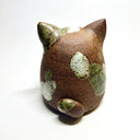 Ceramic sculpture of a cute, brown cat with its paws on its cheek and a rounded bottom without legs. It has green textured spots.