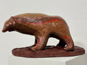 Brown bear figurine with red and yellow accents on a white pedestal against a light gray background