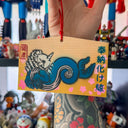 Decorative wooden plaque with a blue wave dragon design and Japanese text, held by a person in a colorful setting.