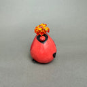 Ceramic sculpture of a very chubby red cardinal bird with black color accents and flowers coming out of its head, with its body being the vase.