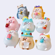 8 different chubby cat figurines, all sitting and holding different accessories. Such as: yarn, gold, toys, milk, a house, etc.