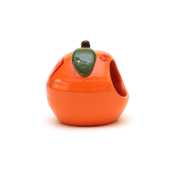 Small ceramic sculpture of an orange or tangerine, with a very short stem and a green leaf. It has decorative red writing on the front and back and a hole carved out of the front.