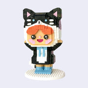 3D sculpture made out of small brick like plastic pieces of a redhead boy wearing a tuxedo with a blue bowtie and with a large black and white cat head around his own, like a hat. He smiles and has his hands both raised up.