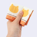 Hand holding a folded up handkerchief with small cat heads on it.