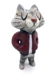 Sculpture of a cartoon gray cat, with closed eyes and a calm expression. It stands like a human and wears a burgundy jacket with its hands in its pockets.