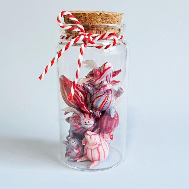 Collection of small sculpture of flying creatures designed to look like striped hard candy in a glass bottle. They are striped white, blue and red.