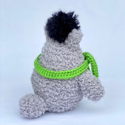 Crochet sculpture of Totoro, with a short rounded body and a green scarf wrapped around his neck, blocking his mouth. Atop his head is a fluffy black dust sprite. Back view.