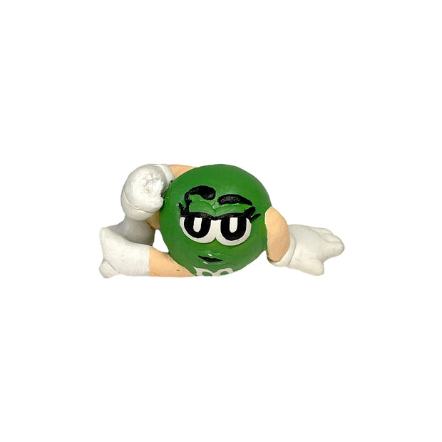 Sculpture of the Green M&M, lounging on the ground with one of her legs positioned up.
