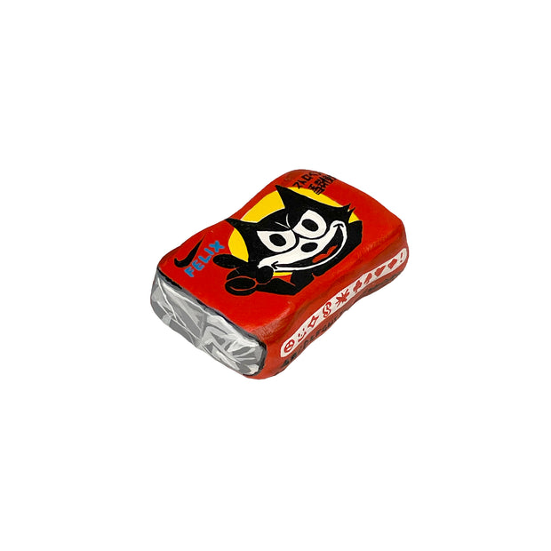Small sculpture of a wrapped piece of square gum with a photo of Felix the Cat on it, looking happy but menacing.