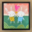 Illustration of 2 cute cartoon style white bunnies, each wearing a patterned dress and smiling. Together, they hold a flower with a large heart ballooning out the middle. They stand in a grassy field with a pink background and green striping pattern along the bottom. Piece is in a black frame.