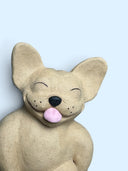 A beige textured dog figurine with a pink tongue sticking out, shown against a solid light blue background.