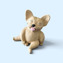 A small beige dog figurine with large upright ears, closed eyes, and a pink tongue sticking out, shown on a light blue background.