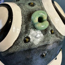 Ceramic sculpture of a small, blowfish with very very large eyes. It is blue with blue fins and green lips. Close up to show textured detailing.