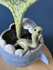 Potted plant shaped like a whale's tail inside of a rounded sculptural pot shaped like a Megladon.