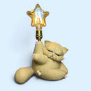 Matte finished ceramic lamp shaped like a very chubby cat with its leg up in the air and a star shaped light bulb at the top of its raised foot.