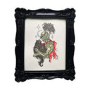 A framed artwork featuring a tattoo-style illustration of a knight in metallic armor holding a black fluffy cat. The knight has a red cape and around them are gold stars on an off-white background, set in an ornate black frame.