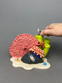 Ceramic sculpture of an under sea theme, with pink and green coral, a sea anemone, stones, fish and various other sea creatures.